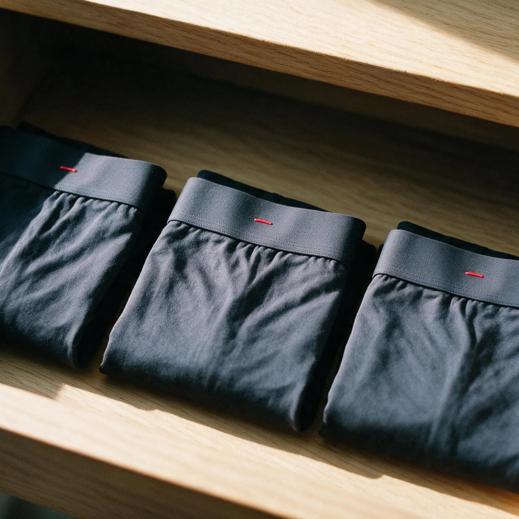 An open walnut drawer of folded ātem boxer-briefs on a dresser